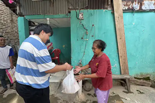 Jasper menyerahkan sekantong bantuan kepada seorang ibu di samping dinding berwarna toska