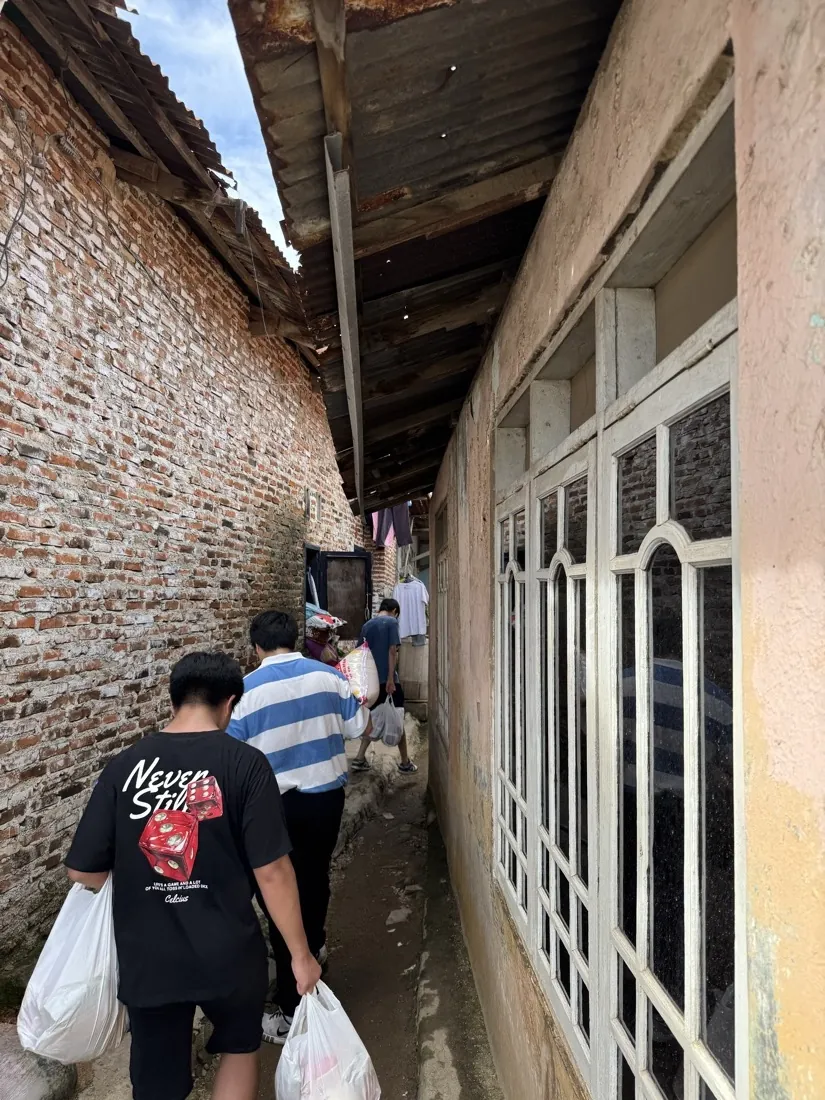 The team walks single file down a narrow alley carrying bags of supplies