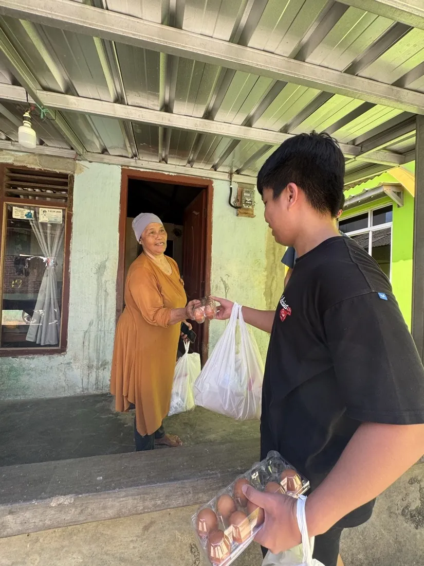 A volunteer hands eggs and a bag of groceries to a woman at her door