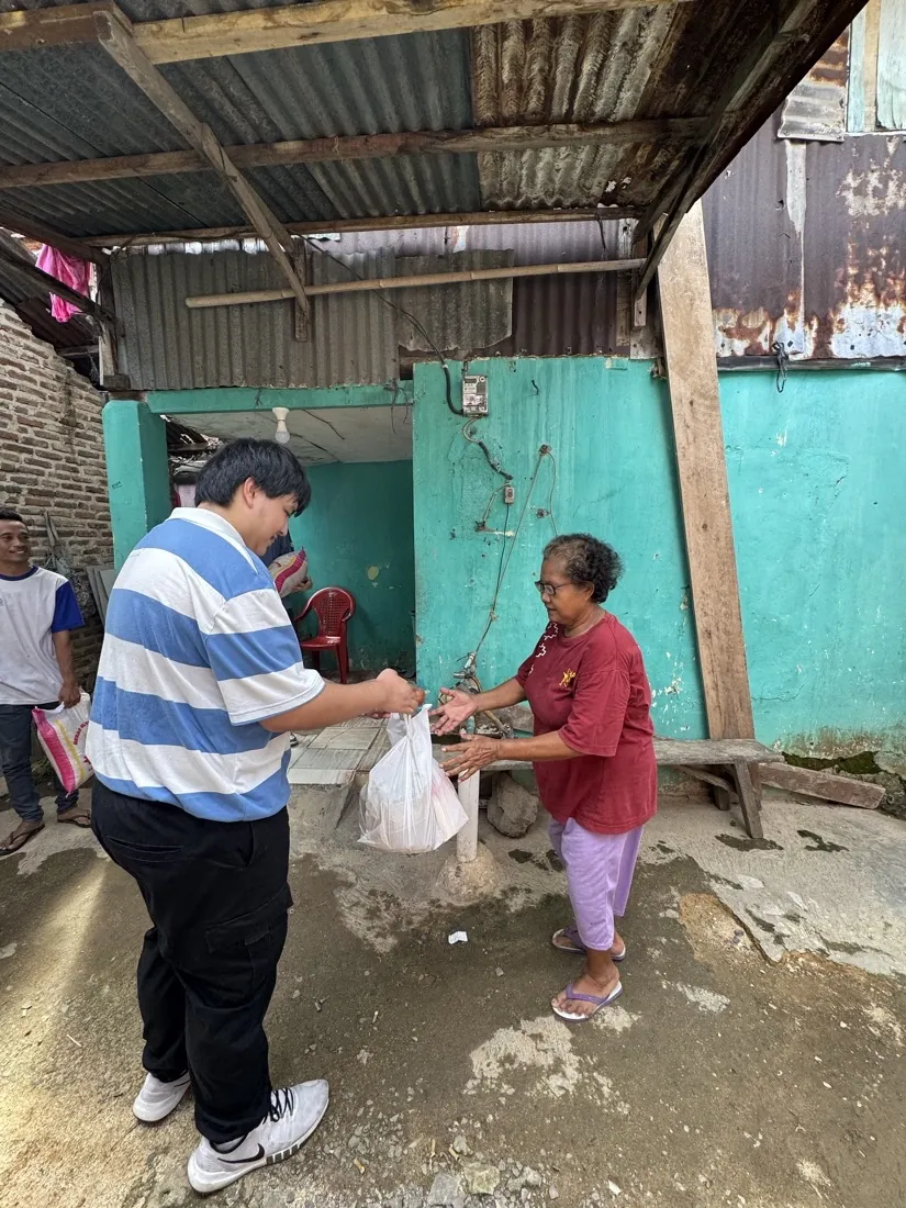 A volunteer hands a bag of supplies to a woman beside a turquoise wall