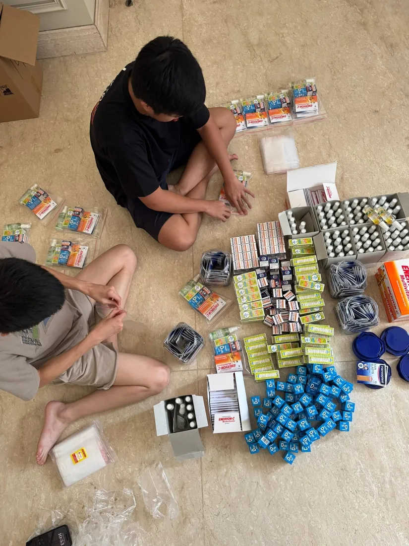 Two volunteers sit on the floor sorting vitamins, sanitizer and medicine into piles