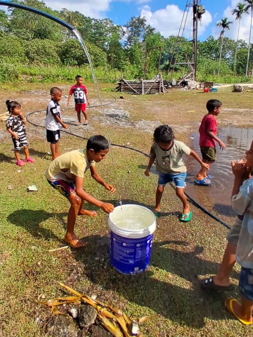 Children gather around a bucket filled with clean water from the new well