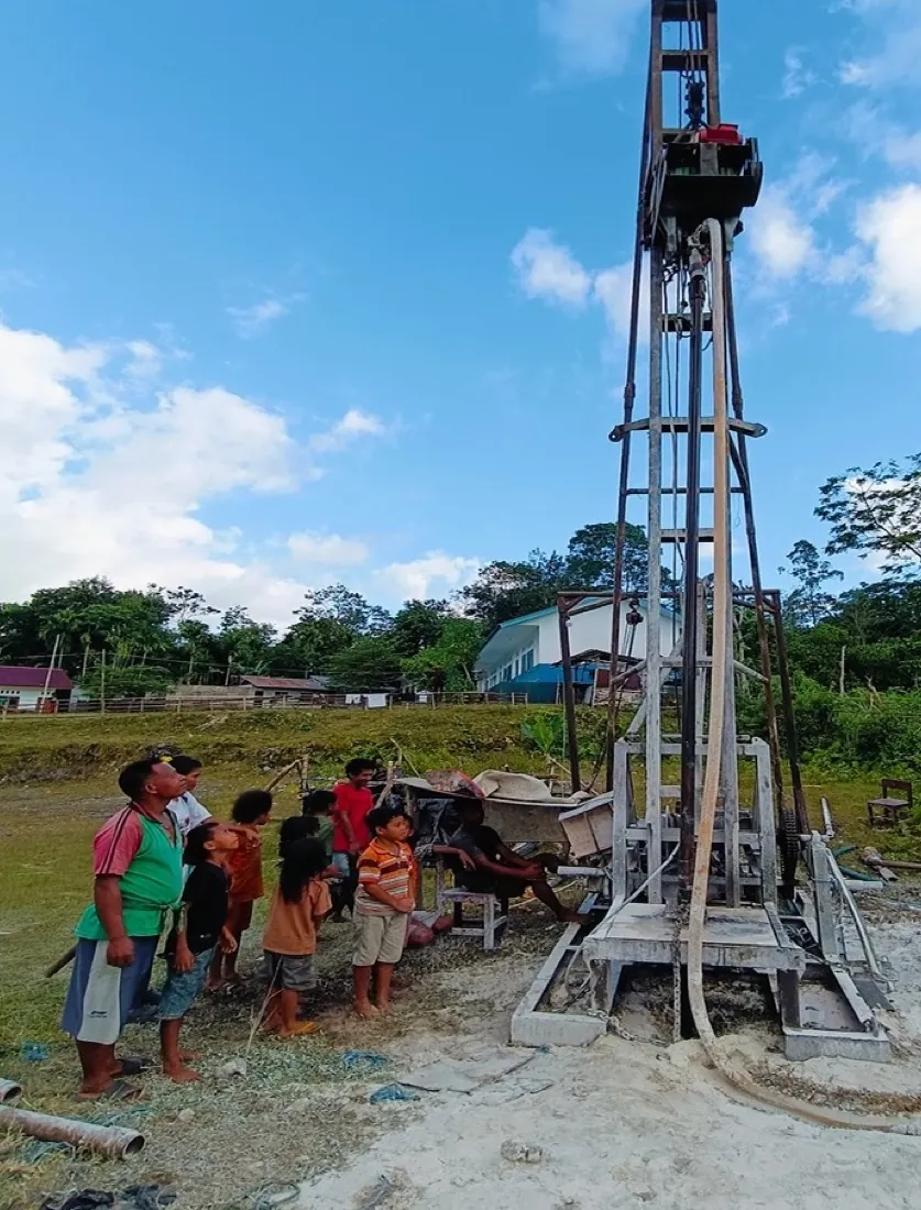 Children and villagers watch as the drilling rig stands over the well site at SD Anugerah