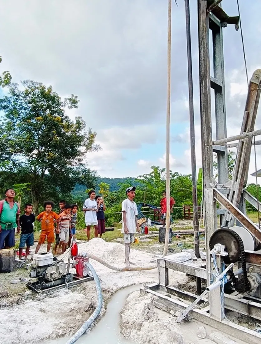 Water pumps through the rig as drilling starts, with families looking on