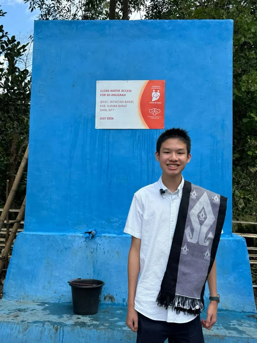 Bryan Wu stands in front of the finished well and its Clean Water Access plaque