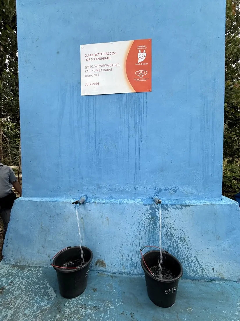 Water runs from both taps of the finished well into buckets below the project plaque