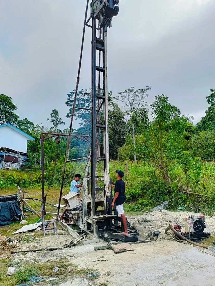 Two workers adjust the drilling rig beside the school